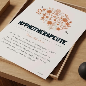Puede incluir: Una impresión enmarcada con la palabra "HYPNOTHÉRAPEUTE" en verde azulado, sobre una definición en francés. La impresión presenta una ilustración floral de un cerebro en naranja y blanco. El marco es marrón claro, sobre una superficie de madera.