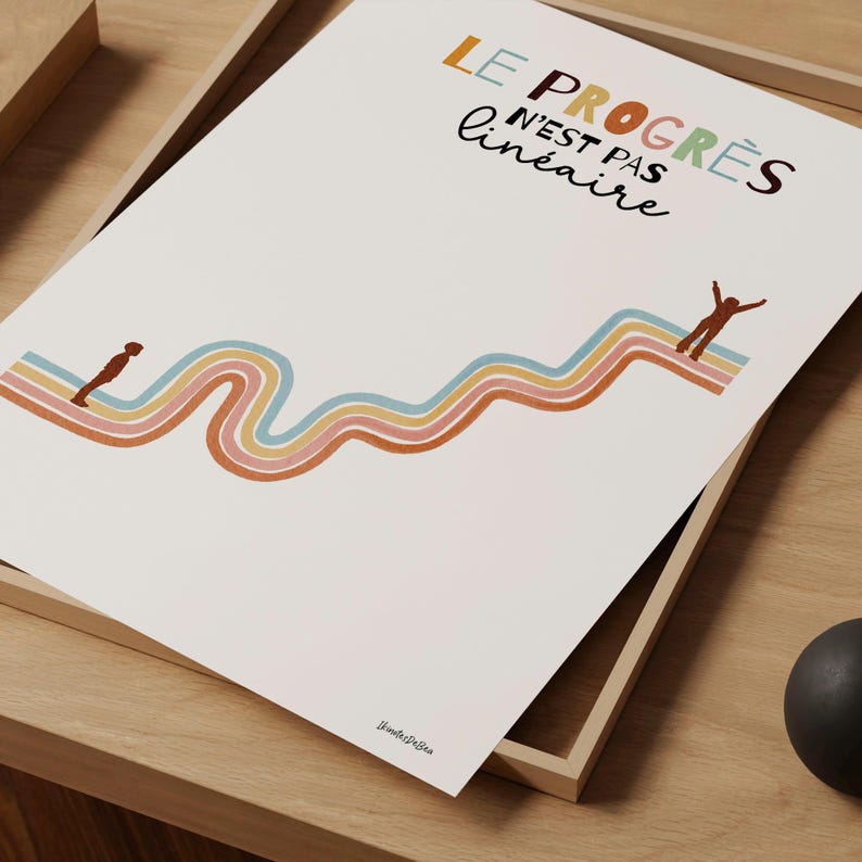 Illustration douce et colorée. Titre : "Le progrès n’est pas linéaire". Une courbe ondulée pastel. En bas, un petit garçon commence son chemin. En haut, un autre atteint un sommet. Le parcours est sinueux, mais porteur d’espoir. Affiche zoomée en grand posée sur un cadre en bois, lui-même posé sur une table.
