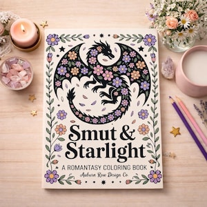 Könnte beinhalten: Ein Malbuch mit dem Titel "Smut & Starlight" mit einem schwarzen Drachendesign, das mit Blumen verziert ist. Das Buch ist von floralen Dekorationen, einer brennenden Kerze, Buntstiften und anderen dekorativen Gegenständen auf einer Holzoberfläche umgeben.