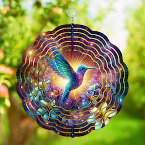Puede incluir: Un adorno de viento decorativo de metal con un vibrante colibrí con plumas iridiscentes azules, moradas y verdes. El diseño incluye un arreglo floral y un fondo celestial, con un lazo para colgar en la parte superior.