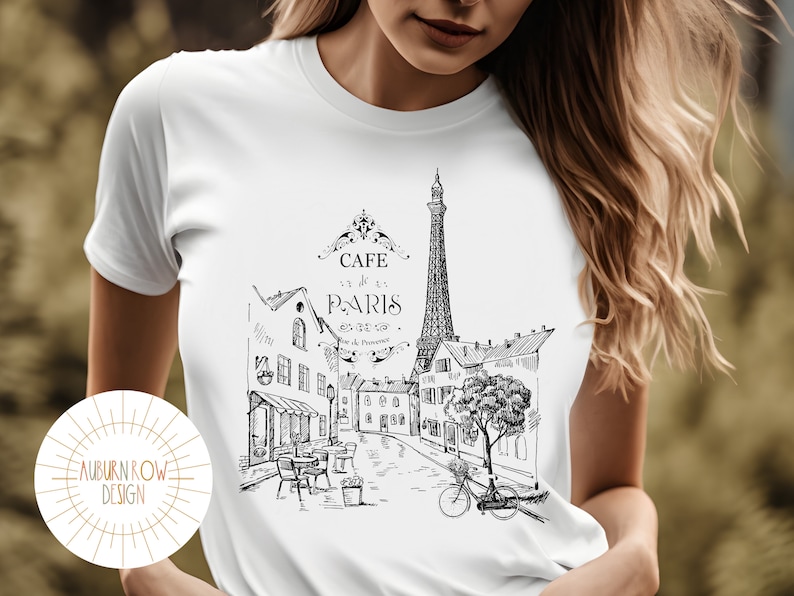 May include: White t-shirt with a black and white illustration of the Eiffel Tower and a Parisian street scene. The text "Cafe de Paris" is printed on the shirt.
