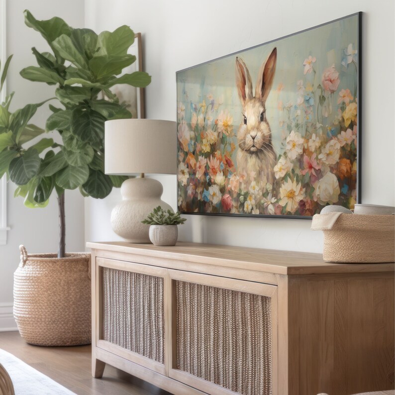 Pu&ograve; includere: Una consolle multimediale in legno marrone chiaro con due ante e un design in rattan intrecciato. La consolle &egrave; decorata con una lampada in ceramica bianca con una base rotonda, una pianta verde in vaso e un dipinto incorniciato di un coniglio in un campo di fiori.
