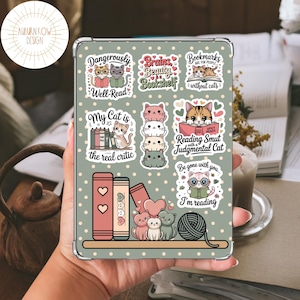 May include: A clear tablet case featuring various cat-themed stickers. The stickers include cats reading books, with phrases like "Dangerously Well-Read" and "Reading Smut." The background is a light green with white polka dots.