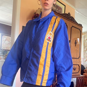 Può includere: Una giacca blu con due strisce gialle sul davanti e una toppa con una bandiera canadese e le parole "Royal Canadian Mounted Police" sul lato sinistro.