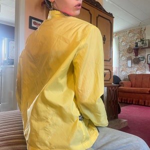 May include: A yellow, lightweight jacket with a zipper closure. The jacket is made of a smooth, silky fabric and has a relaxed fit.