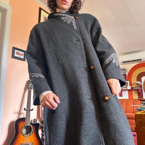 Peut inclure: Un long manteau gris foncé avec un col montant et de gros boutons en bois. Le manteau présente des coutures décoratives de couleur gris clair le long du col et des manches. Le manteau est de style vintage, adapté au temps froid.