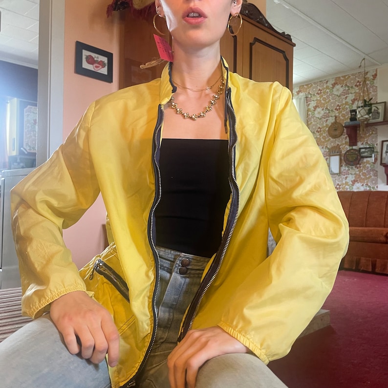 May include: A yellow jacket with a zipper closure and a black top underneath. The jacket has a zippered pocket on the left side.