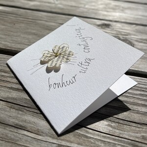 Carte pour souhaiter du bonheur.
Carte double blanche 9x9 cm et son enveloppe. un trèfle à 4 feuilles est fixé par un fil doré, sous lequel est écris: bonheur ultra contagieux ! la phrase suit le contour du trèfle et s'envole.