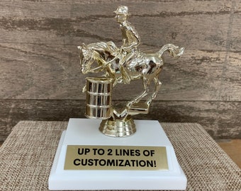 May include: Gold-colored trophy featuring a rider on a horse jumping over a barrel. The base of the trophy is white with a gold plaque that reads "UP TO 2 LINES OF CUSTOMIZATION!"