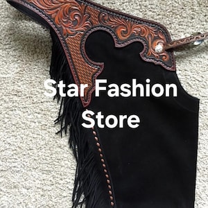 May include: Black suede chaps with brown tooled leather accents. The chaps feature a decorative floral pattern on the yoke and fringe along the side. The text "Star Fashion Store" is visible on the chaps.