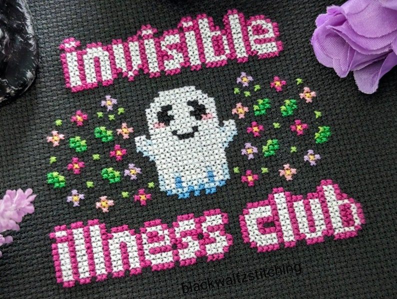 Puede incluir: Dise&ntilde;o de punto de cruz sobre tela negra con un fantasma sonriente con las palabras "Invisible Illness Club" e "Invisible" en rosa y blanco. El fantasma est&aacute; rodeado de flores coloridas.