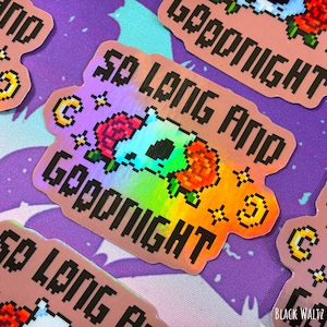 May include: Holographic sticker with the text "So Long and Goodnight" in pixelated font. The sticker features a pixelated skull with roses, moons, and stars. The background is a purple fabric with a bat pattern.