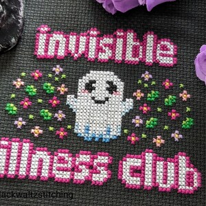 Puede incluir: Dise&ntilde;o de punto de cruz sobre tela negra con las palabras "invisible illness club" en rosa y blanco. Un fantasma sonriente est&aacute; rodeado de flores coloridas. El nombre del artista, "blackwaltzstitching", est&aacute; en la parte inferior.
