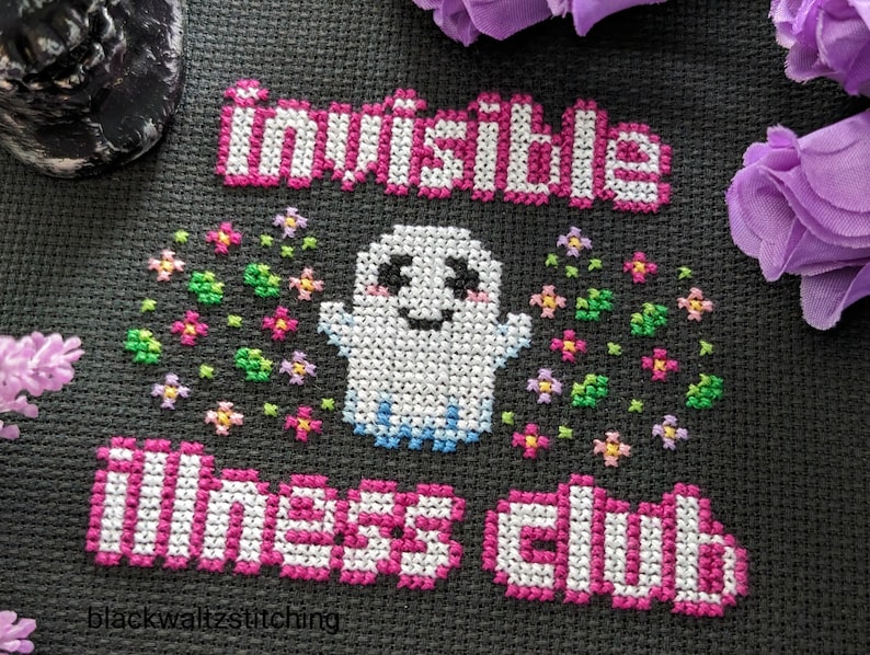 Puede incluir: Dise&ntilde;o de punto de cruz sobre tela negra con las palabras "invisible illness club" en rosa y blanco. Un fantasma sonriente est&aacute; rodeado de flores coloridas. El nombre del artista, "blackwaltzstitching", est&aacute; en la parte inferior.