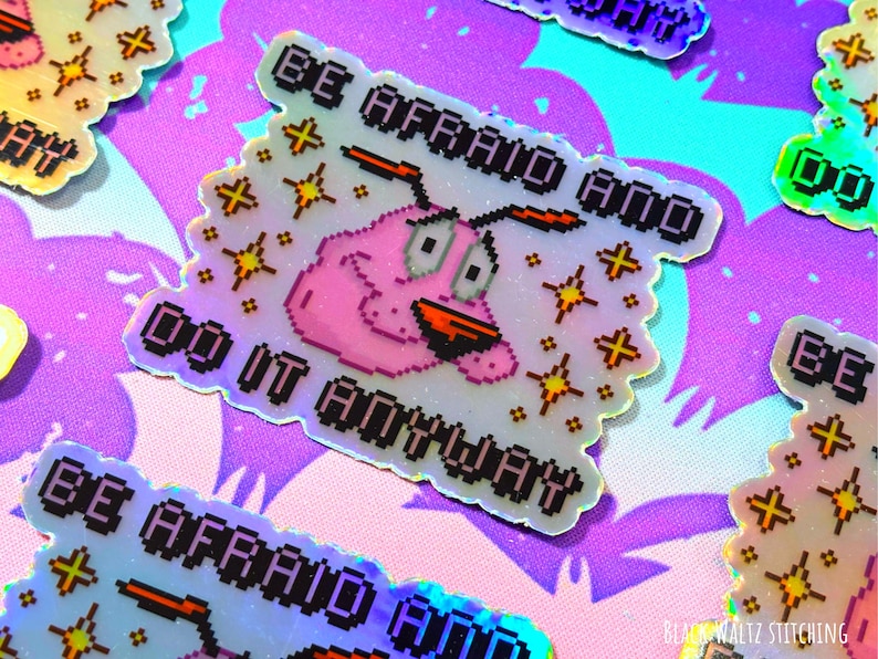 Puede incluir: Pegatinas hologr&aacute;ficas con la frase "BE AFRAID AND DO IT ANYWAY" y una imagen pixelada de Coraje, el perro cobarde. Las pegatinas tienen un borde festoneado y est&aacute;n dispersas sobre un fondo morado y azul estampado.