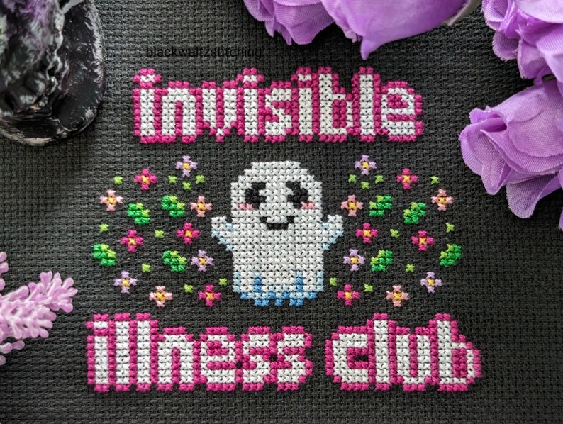Puede incluir: Dise&ntilde;o de punto de cruz sobre tela negra con las palabras "Invisible Illness Club" en rosa y blanco. Un fantasma sonriente est&aacute; rodeado de flores coloridas. La palabra "invisible" est&aacute; en la parte superior.