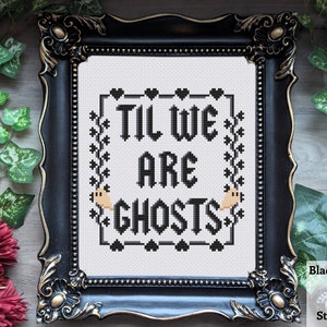 May include: A black framed cross-stitch with white fabric and black embroidery. The embroidery reads "Til We Are Ghosts" with a small ghost on each side of the text.