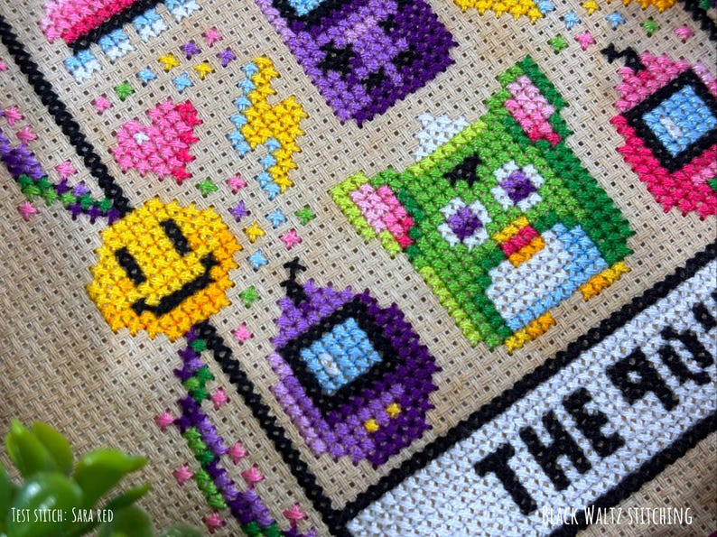 May include: Close-up of a cross-stitch design featuring colorful pixelated characters and shapes. The design includes a yellow smiley face, a green creature, and purple and pink geometric shapes. The text "THE 90'S" is visible.