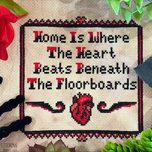 May include: A cross-stitch embroidery on beige fabric featuring the black and red text "Home Is Where The Heart Beats Beneath The Floorboards" with a central anatomical heart graphic, enclosed in a decorative black and red stitched border.