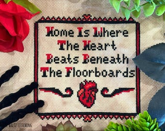 May include: A cross-stitch embroidery on beige fabric featuring the black and red text "Home Is Where The Heart Beats Beneath The Floorboards" with a central anatomical heart graphic, enclosed in a decorative black and red stitched border.