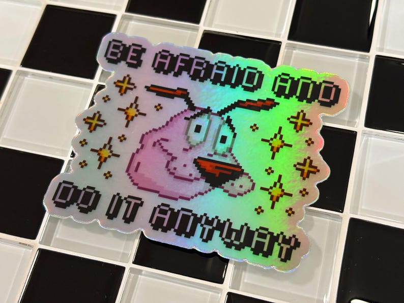 Puede incluir: Pegatina hologr&aacute;fica con Coraje, el perro cobarde, y el texto "BE AFRAID AND DO IT ANYWAY". La pegatina tiene un dise&ntilde;o pixelado, con un perro rosa y acentos de estrellas amarillas. El fondo es un patr&oacute;n de tablero de ajedrez en blanco y negro.