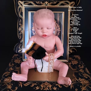 May include: A crochet drawstring bag featuring black, brown, and white stripes with a shell edge, measuring 3 by 4 inches. The bag is accompanied by a gold-tone metal bracelet with clear rhinestones, displayed with a doll figure.