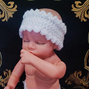 May include: A white crocheted headband with a scalloped edge. The headband is worn by a baby doll.