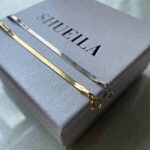 May include: Two gold and silver chain necklaces on a white box with the word "SHUEILA" printed on it.