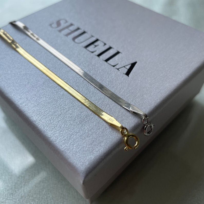 May include: Two gold and silver chain necklaces on a white box with the word "SHUEILA" printed on it.