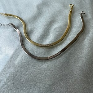 May include: Two gold and silver snake chain necklaces with engraved messages. The gold necklace says "Patience is key" and the silver necklace says "Never Give Up".