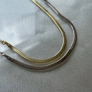 May include: Two gold and silver snake chain necklaces with engraved messages. The gold necklace says "Patience is key" and the silver necklace says "Never Give Up".