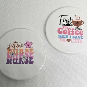 May include: A white ceramic mug with a black handle and the text "But First, Coffee" in a bold, black font. The mug is set against a blurred background, suggesting a cozy setting.