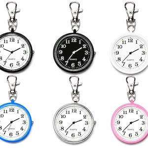 May include: Six round quartz fob watches with lobster claw clasps. The collection includes one black case with a white face, one black case with a black face, one white case with a white face, one blue case, one silver case, and one pink case.