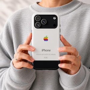 Puede incluir: Una funda de smartphone blanca y negra con un logotipo de Apple de colores arcoíris retro en el centro, la palabra iPhone impresa debajo y un recorte para el módulo de cámara en la parte superior. Incluye detalles de texto y una etiqueta de 8 GB.