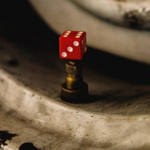 May include: A red die with white dots sits on top of a gold metal valve stem. The die is a common accessory for car enthusiasts.
