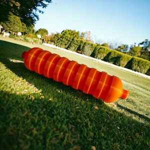 May include: An orange, expandable, cylindrical buoy made of plastic. The buoy is lying on a green grassy lawn.