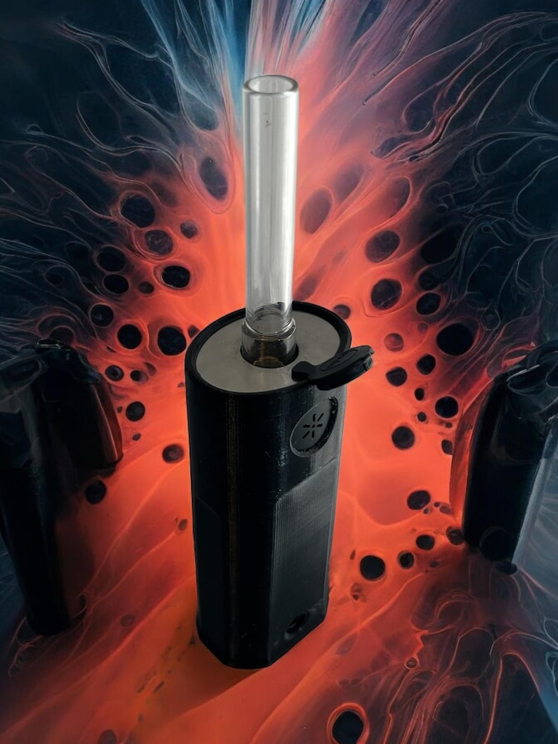 May include: A black and silver vaporizer with a glass mouthpiece. The vaporizer is sitting on a red and black background.