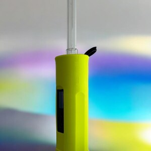 May include: A bright yellow electronic vaporizer with a clear glass mouthpiece and a black lid. The vaporizer is standing on a reflective surface.