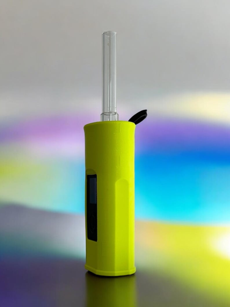 May include: A bright yellow electronic vaporizer with a clear glass mouthpiece and a black lid. The vaporizer is standing on a reflective surface.