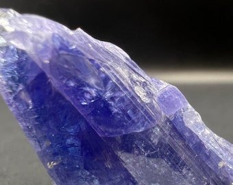 May include: A deep blue, faceted, crystal specimen with a translucent, glassy appearance. The crystal has a sharp, pointed shape and is arranged in a layered formation.