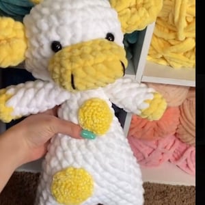Puede incluir: Animal de peluche blanco de crochet con forma de vaca con orejas, nariz y manchas amarillas. La vaca está de pie sobre una superficie marrón.