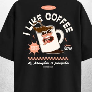 May include: Black t-shirt with a coffee-themed graphic. The design features a cartoon coffee mug with the text "I Like Coffee" and "& Maybe 3 people". Additional text includes "Brew Crew" and "Join Now!"