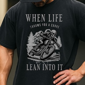 May include: Black t-shirt with a graphic of a skeleton riding a motorcycle, with the text "WHEN LIFE throws you a curve LEAN INTO IT". The design is in shades of gray and white.