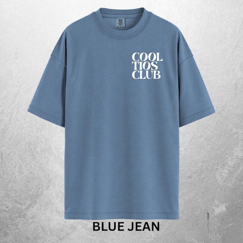 May include: A blue jean colored t-shirt with the text "COOL TIOS CLUB" in white on the front. The shirt has a crew neck and short sleeves. The words "BLUE JEAN" are printed in white at the bottom of the shirt.