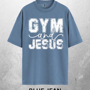 May include: Blue jean colored t-shirt with the words "GYM and JESUS" in distressed white lettering. The shirt has short sleeves and a crew neck. The words "BLUE JEAN" are printed at the bottom of the shirt.