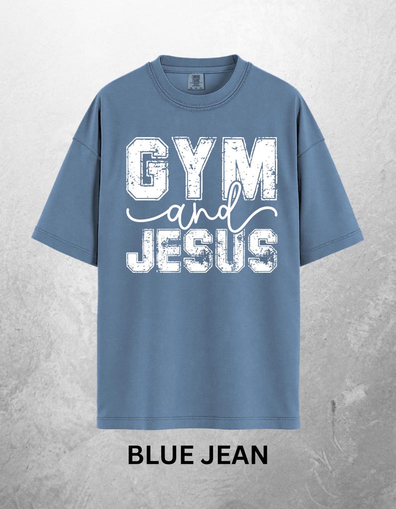 May include: Blue jean colored t-shirt with the words "GYM and JESUS" in distressed white lettering. The shirt has short sleeves and a crew neck. The words "BLUE JEAN" are printed at the bottom of the shirt.