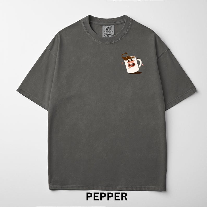 May include: A dark gray t-shirt with a crew neck and short sleeves. The shirt features a small graphic of a smiling coffee mug with brown coffee and pink accents. The word "PEPPER" is printed at the bottom.