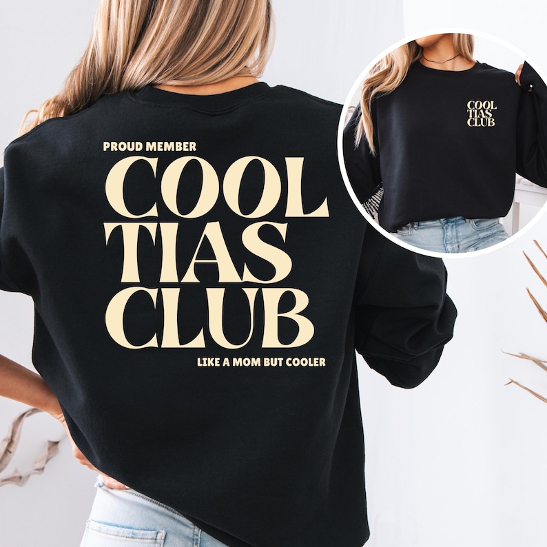 May include: Black sweatshirt with the text "COOL TIAS CLUB" in a cream-colored font. The text "PROUD MEMBER" is above the main text, and "LIKE A MOM BUT COOLER" is below. A smaller version of the text is on the sleeve.