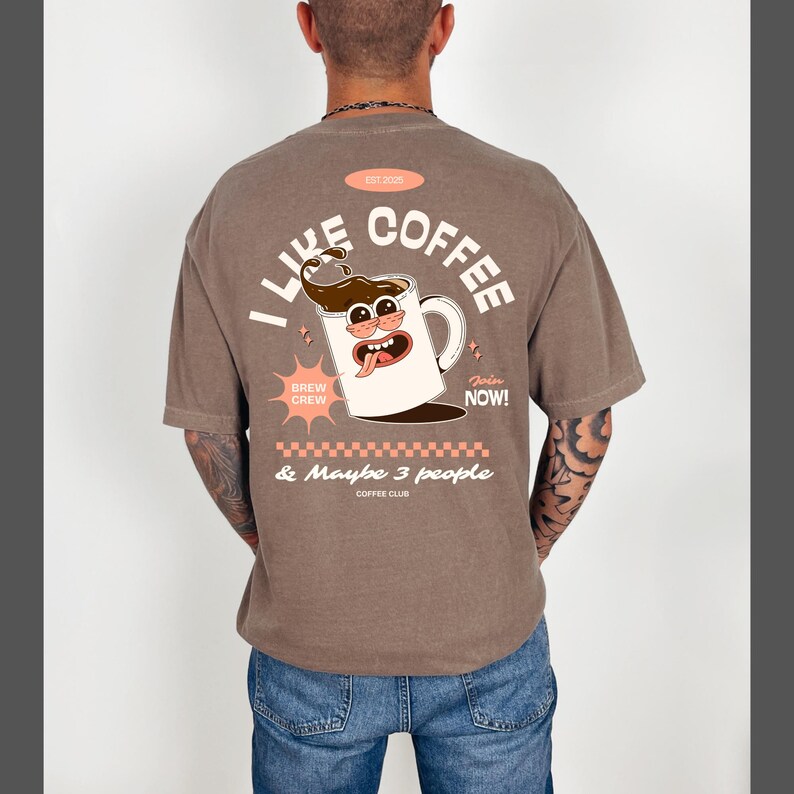 May include: Brown t-shirt with a coffee-themed graphic on the back. The design features a cartoon coffee cup with the text "I LIKE COFFEE & Maybe 3 people". Additional text includes "BREW CREW" and "Join NOW!"