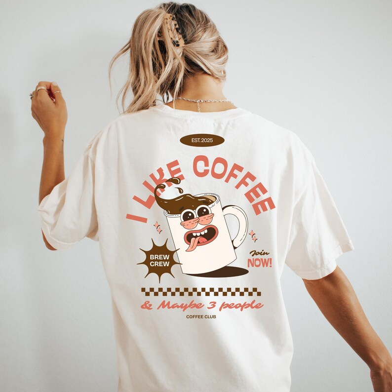 May include: Cream-colored t-shirt with a retro coffee-themed graphic. The design features a cartoon coffee mug with a face, the text "I Like Coffee" and "Brew Crew". The shirt also has the text "& Maybe 3 people" and "Coffee Club".